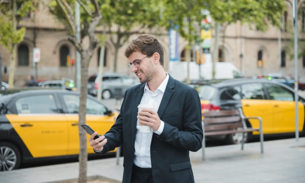 hombre de negocios joven que sostiene la taza de cafe que mira el telefono movil